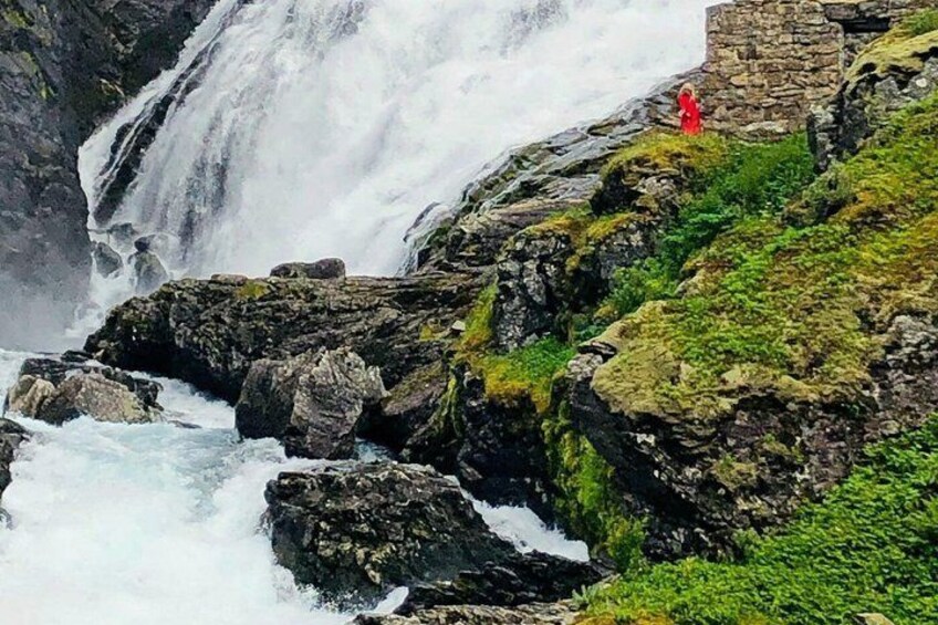 A waterfall cascading over rocks, a person in red, and a stone structure. 5