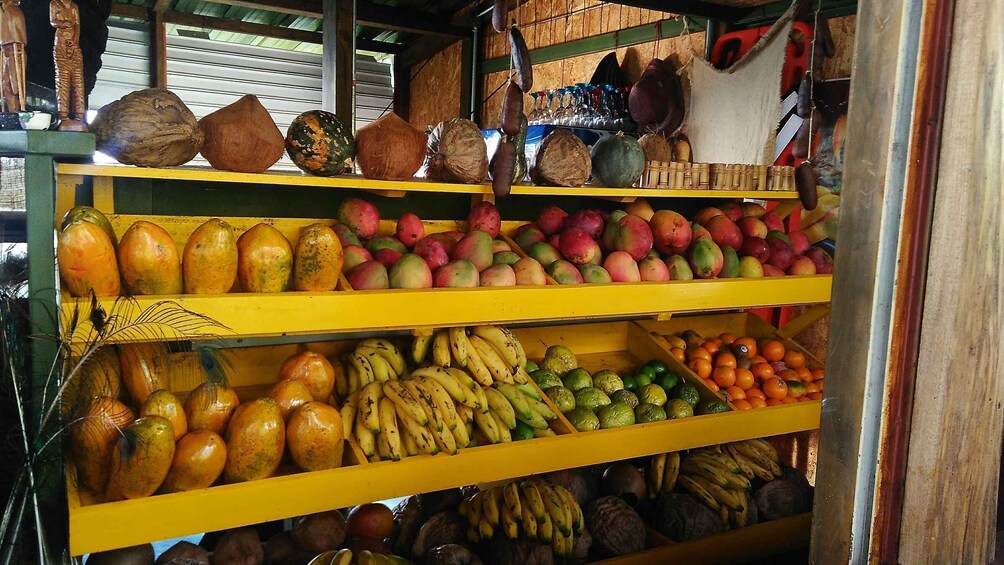 A fruit stand with various fruits and coconuts on yellow shelves. 2