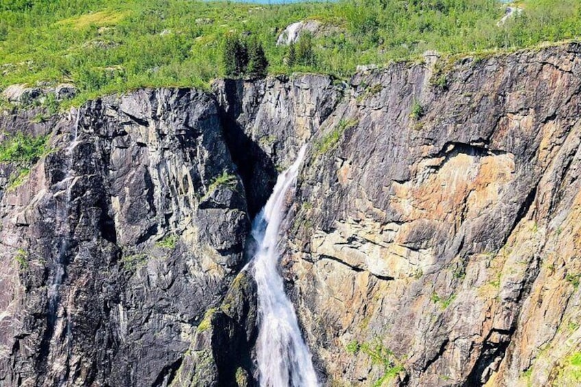 A waterfall cascading down a rocky cliff surrounded by greenery. 2