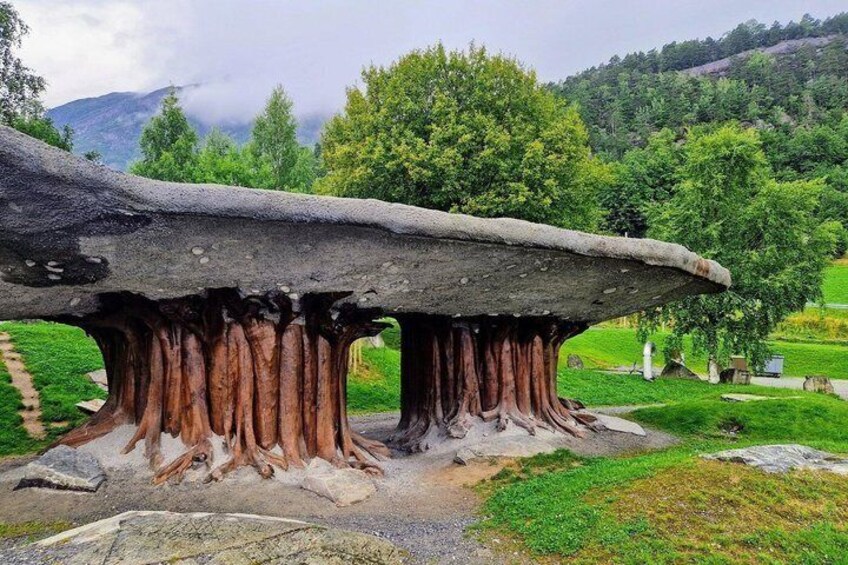 A large rock formation with a flat top and roots extending into the ground. 3