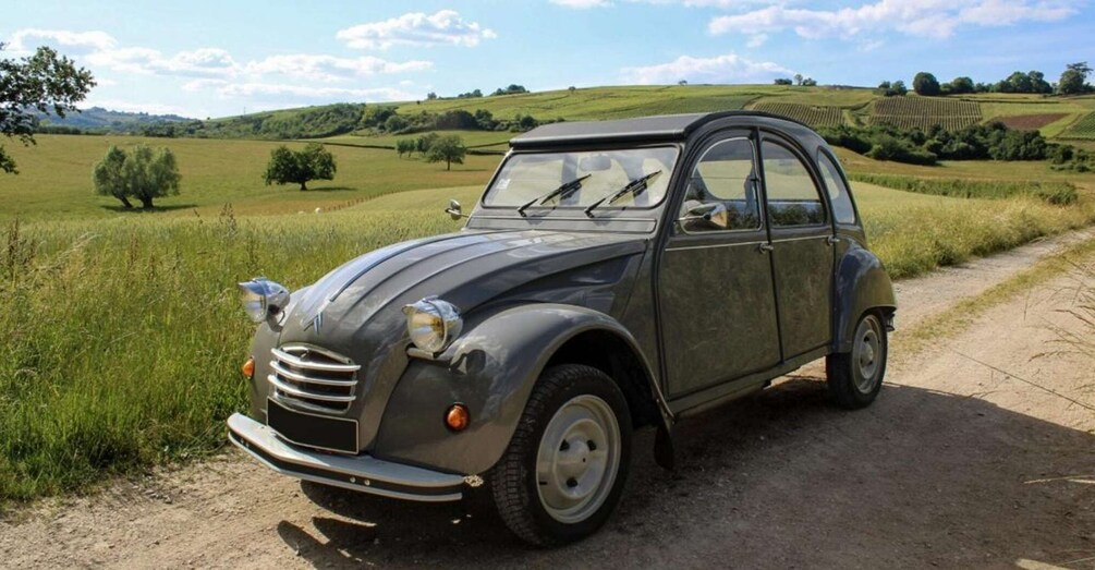 A vintage car parked on a rural dirt road with fields and hills in the background. 2