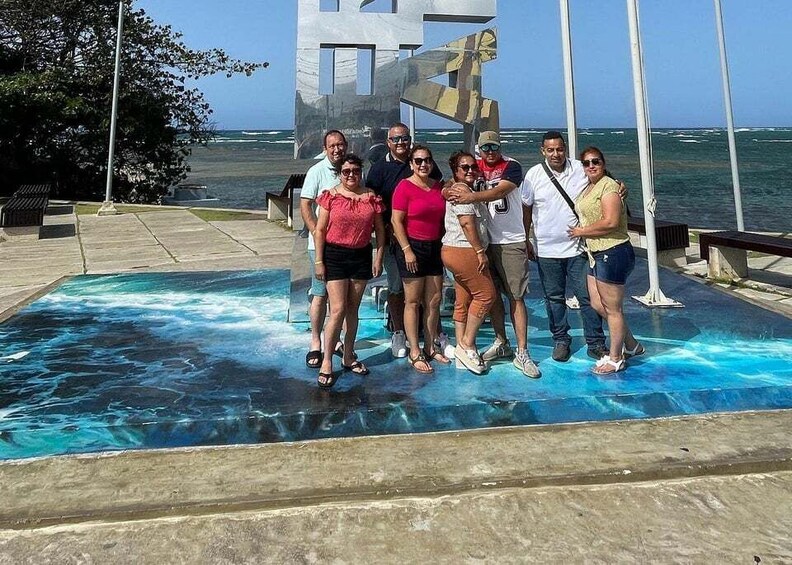 A group of people standing on a glass-bottomed pool with a view of the ocean and a large sculpture in the background. 5