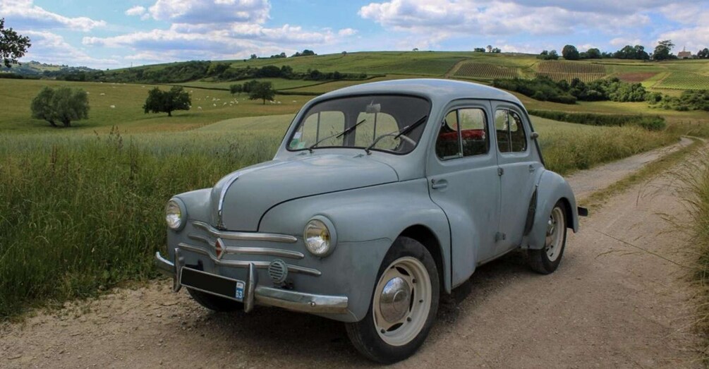 A vintage car parked on a rural dirt road with fields and hills in the background. 5