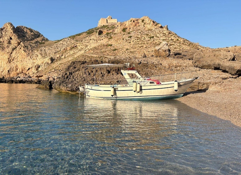 A boat docked at a rocky shoreline with a fortress on a hill in the background. 1