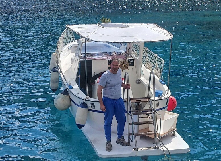 A man standing on a small boat with a canopy, floating on calm blue water. 2