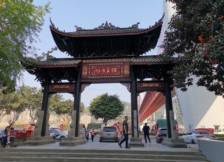 A traditional Chinese gate with intricate designs and characters, set in an urban park with trees and parked cars. 4
