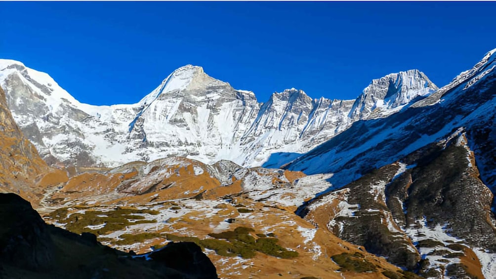 A mountain range with snow-covered peaks and a valley with exposed rock and sparse vegetation. 1