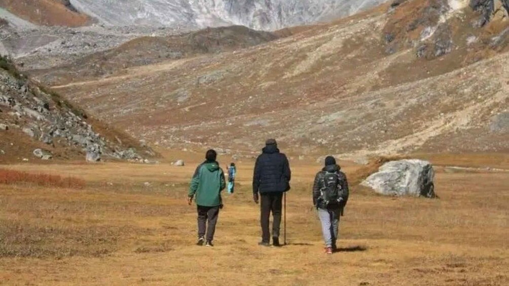Three people walking on a grassy field with a rocky mountain in the background. 3
