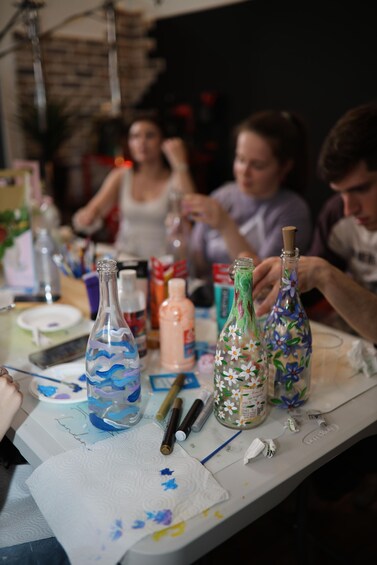 A table with painted glass bottles, paintbrushes, and art supplies. 5