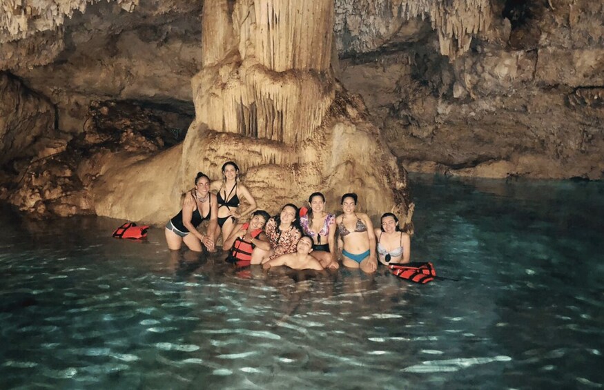 A group of people in a cave pool with clear water, surrounded by rocky formations and a large stalactite. 2