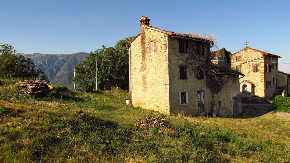 An old stone building with a red-tiled roof, surrounded by grass and trees, with mountains in the background. 4