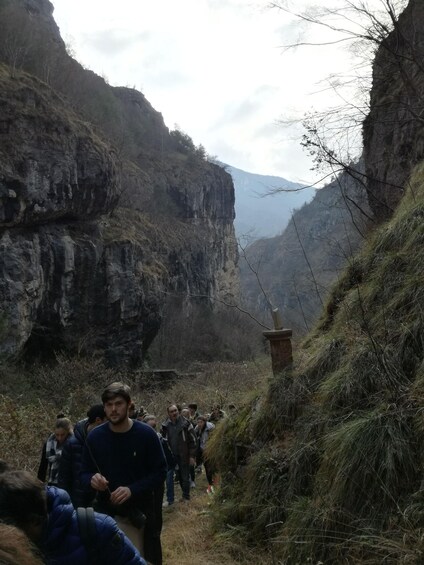 A group of people hiking on a narrow mountain trail surrounded by steep cliffs. 2