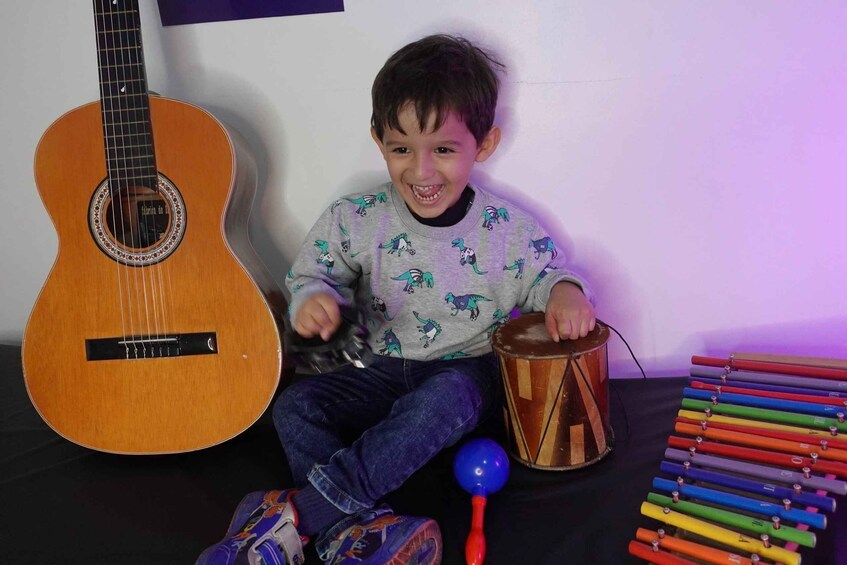 A child sitting with a guitar, drum, and colorful xylophone. 2