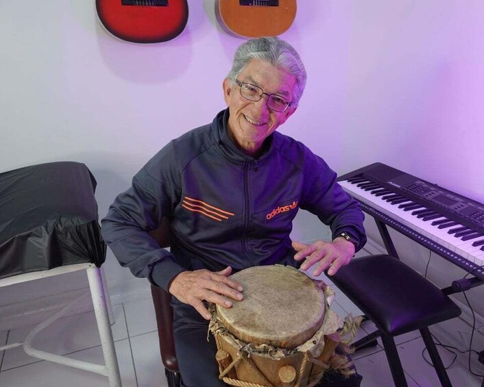 A person playing a drum in a room with a keyboard and a guitar in the background. 4