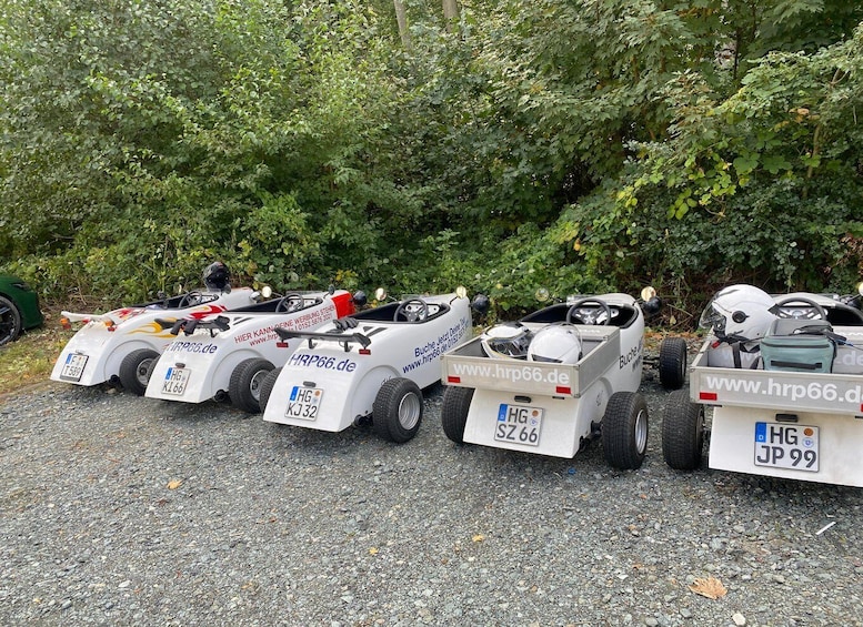 A row of small, white remote-controlled cars parked on a gravel surface with license plates and website URLs visible. 1