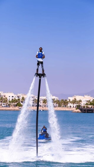 A person jet-skiing on a water jetpack, with a jetpack operator on a stand above. 2