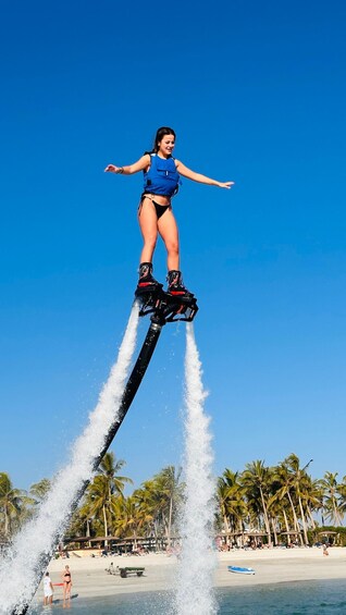 A person performing a water jetpack stunt over a beach with palm trees and a clear sky. 3