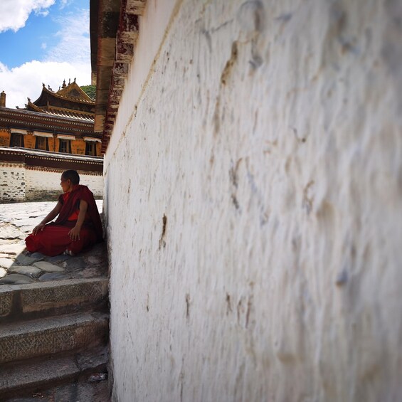 A person in red sitting on stone steps in front of a white wall with a traditional building in the background. 4