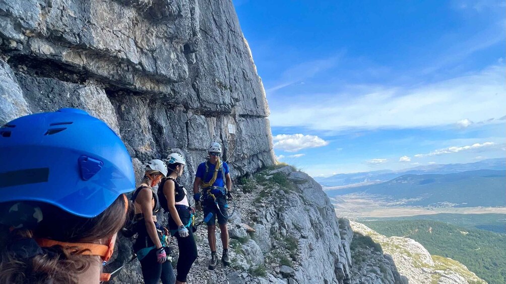A group of people rappelling down a rocky cliff with a scenic valley in the background. 5