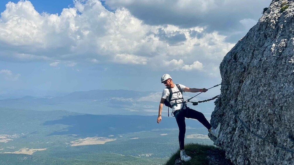 A person rappelling down a rocky cliff with a mountainous landscape in the background. 3