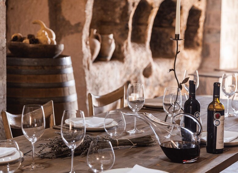 A rustic dining table set with wine glasses, plates, and bottles, with a stone wall and pottery in the background. 5