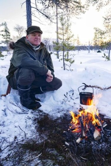 A person crouching next to a campfire in a snowy forest. 3