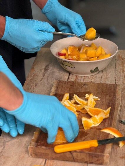 A person wearing blue gloves preparing fruit, specifically cutting and scooping mangoes into a bowl. 4