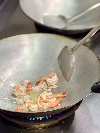 A wok on a stove with shrimp cooking. 3
