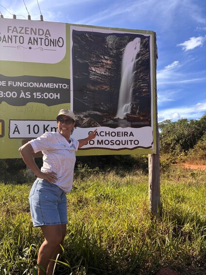 A person standing next to a signboard with a waterfall and a label 'Cachoeira do Mosquito'. 2