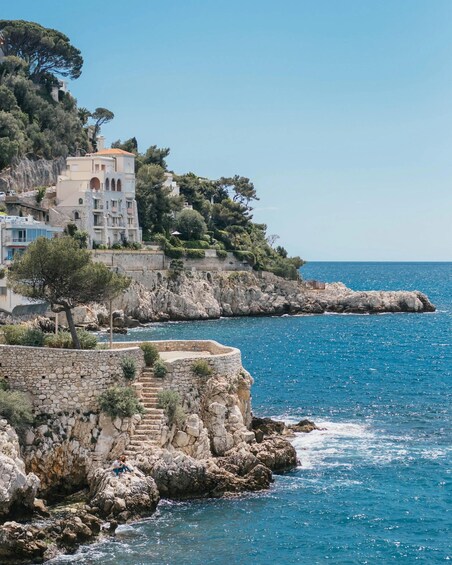 A coastal town with stone buildings, a clear blue sea, and rocky cliffs. 5