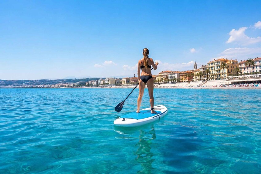 A person paddleboarding on clear blue water with buildings in the background. 1