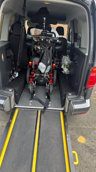 Espacio de carga de un vehículo con una rampa para silla de ruedas, un scooter de movilidad rojo y una mochila. 4