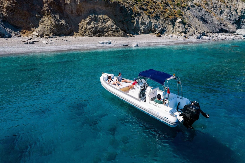 A boat with passengers on a clear turquoise sea, rocky coastline, and a sandy beach in the background. 3