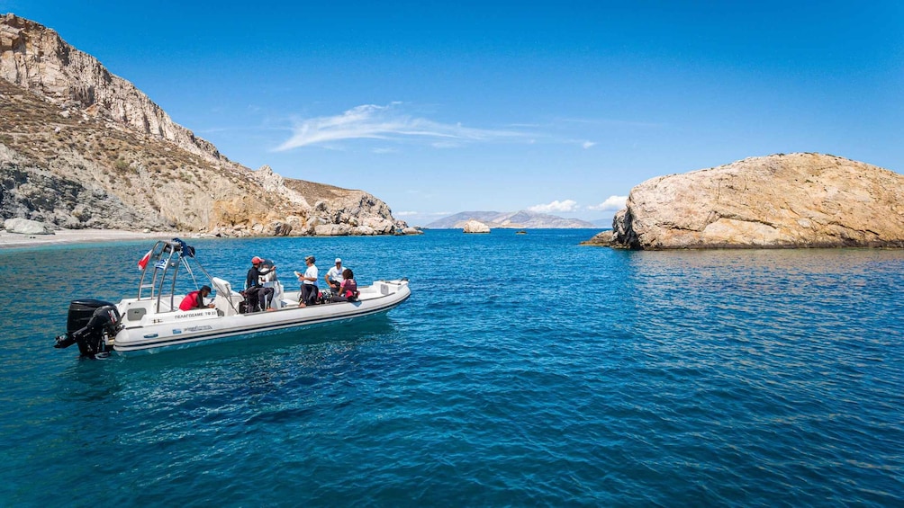 A boat with people on a clear blue sea, rocky cliffs, and distant mountains. 5