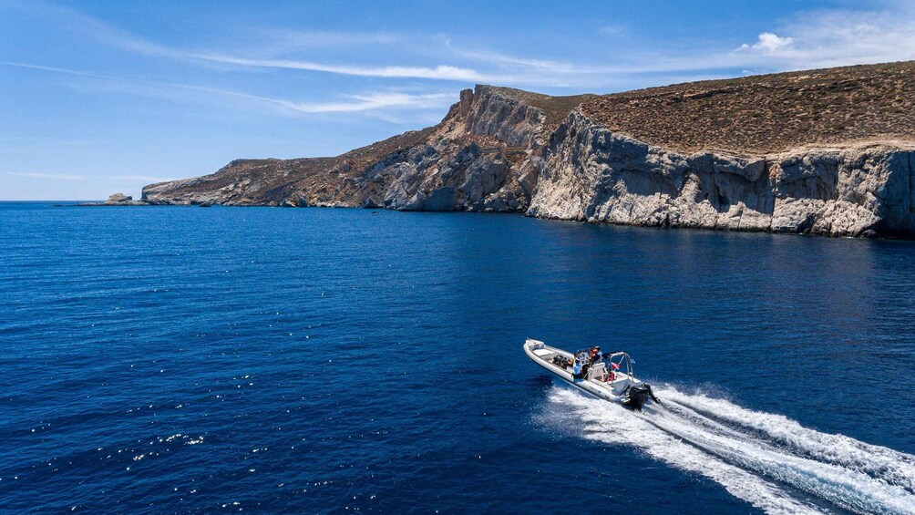 A speedboat on a clear blue sea with rocky cliffs in the background. 2