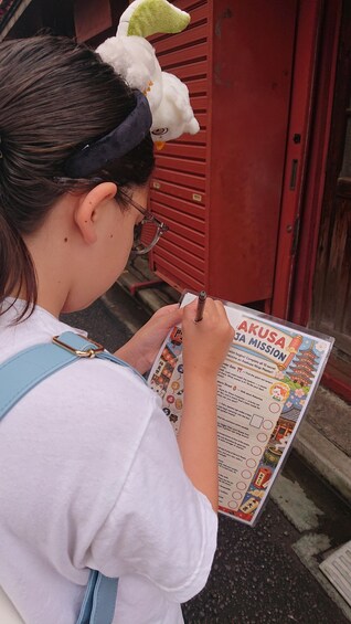 A person holding a booklet titled 'AKUSA JA MISSION' with a list of tasks. 4