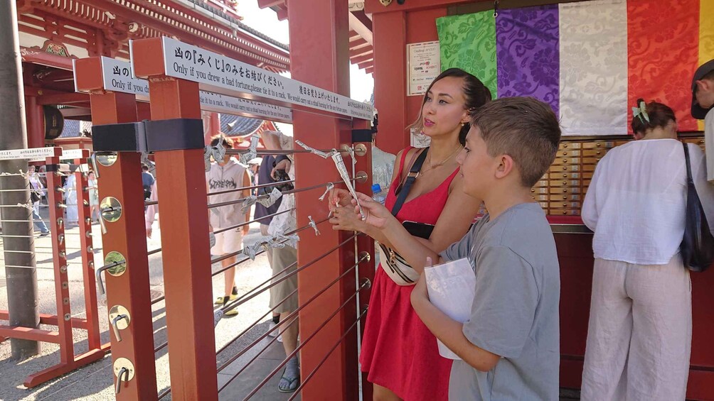 A traditional Japanese gate with a sign in Japanese, a person tying a rope, and a colorful banner in the background. 2