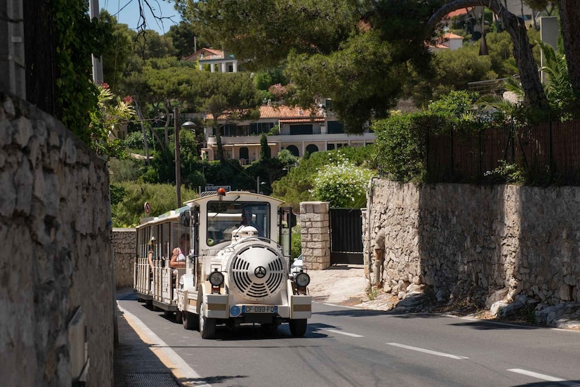 A vintage tram with passengers, traveling on a road flanked by stone walls and trees. 2