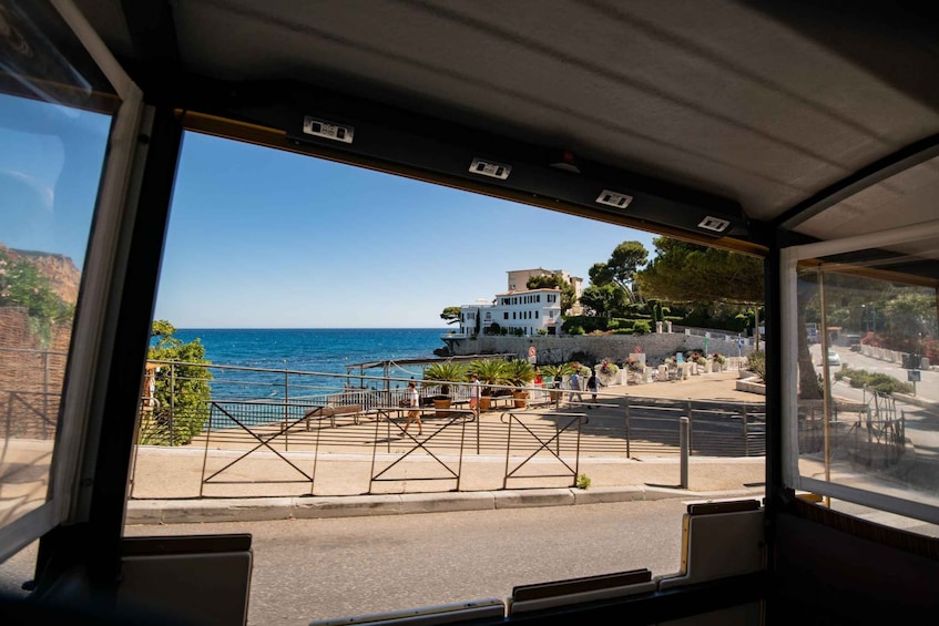 A coastal view from inside a vehicle, with a building, promenade, and sea in the background. 4