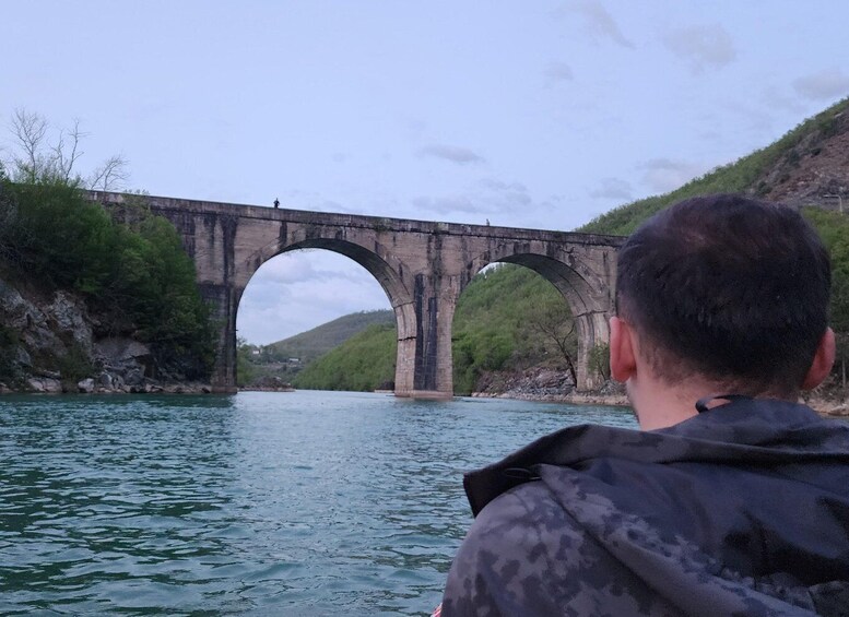 A man in a boat looking at a stone bridge over a river. 2