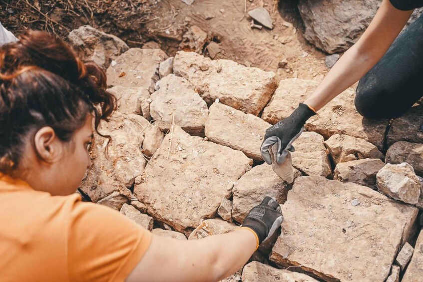 A person placing a large rock on a rocky surface. 3