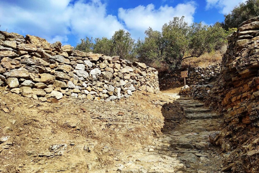 A stone pathway leading through a rocky terrain with a stone wall on one side and a signpost in the distance. 1
