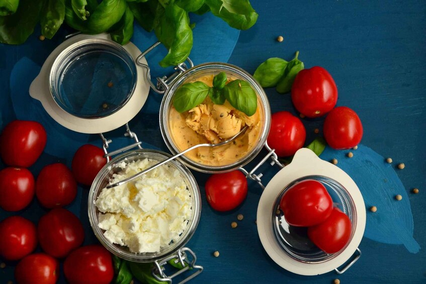 A blue surface with jars of food, including tomatoes and a creamy substance, and fresh basil leaves. 1