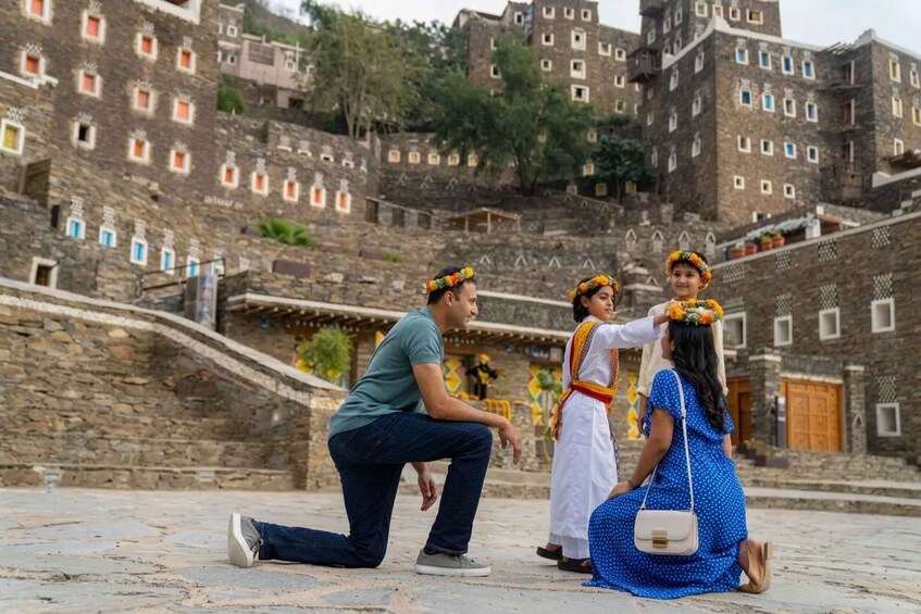 A group of people in traditional attire with a historic stone building in the background. 1