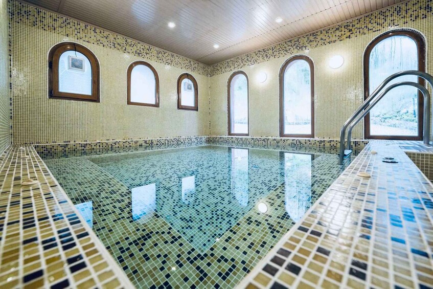 A large indoor swimming pool with mosaic tile walls and arched windows. 3