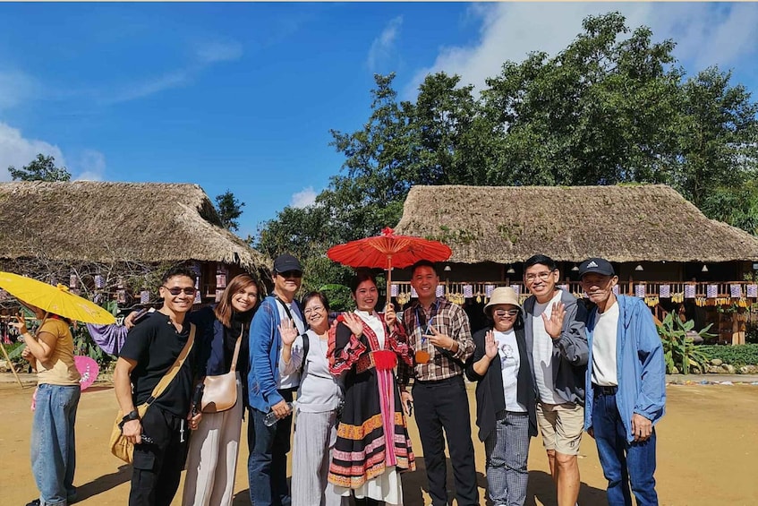 A group of people posing in front of thatched-roof structures with trees in the background. 5