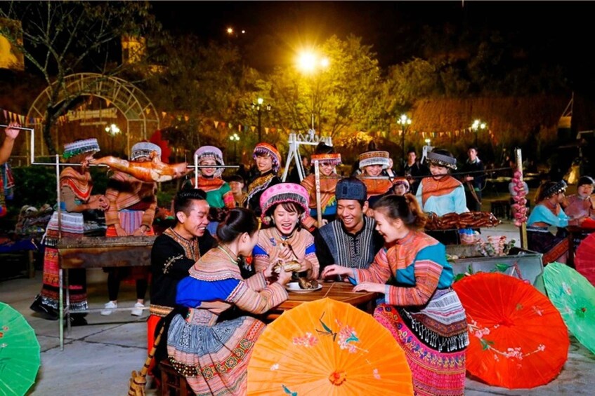 A group of people in traditional attire seated around tables, engaged in a social gathering outdoors at night. 2