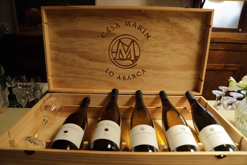 A wooden wine box with 'CASA MARIN LO ABARCA' engraved on the lid, containing several wine bottles and glasses. 5