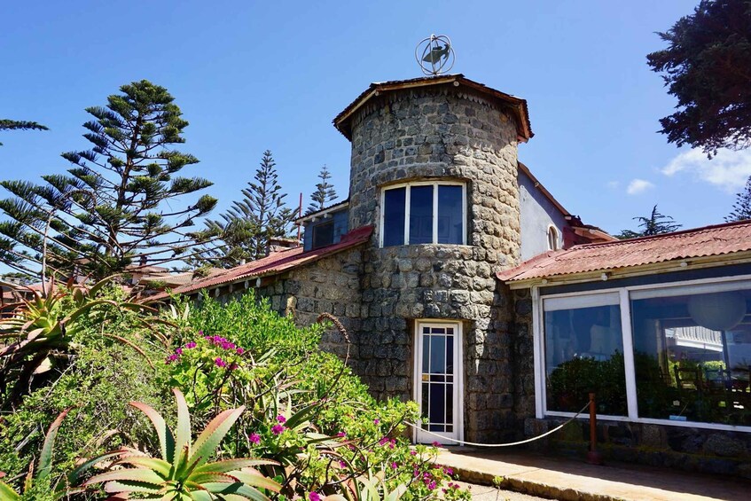A stone building with a red roof, surrounded by lush greenery and a clear blue sky. 1