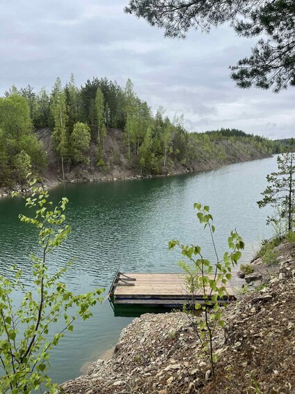 A calm river with a wooden dock extending into the water, surrounded by dense trees and a rocky shoreline. 1
